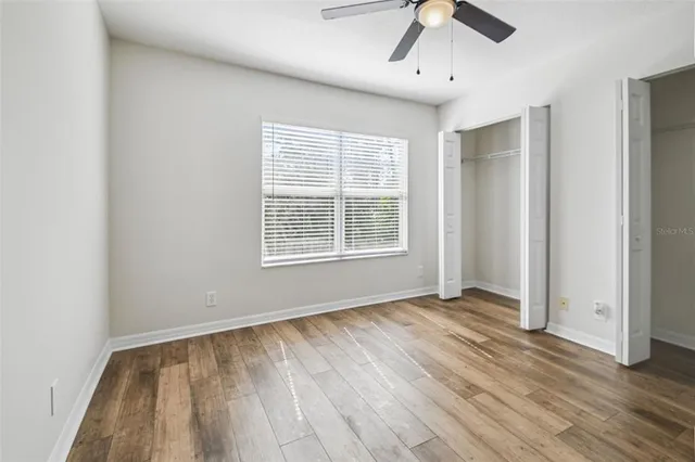 an empty room with wooden floor chandelier fan and windows