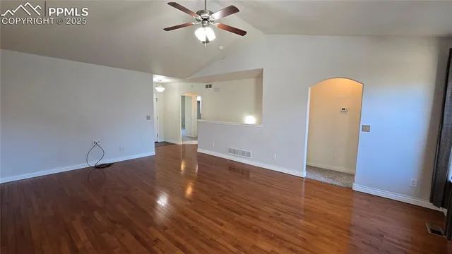 a view of an empty room with wooden floor and a ceiling fan
