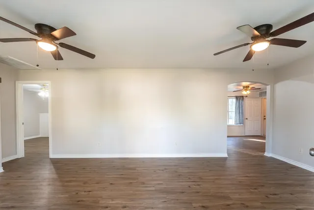 an empty room with wooden floor ceiling fan and windows