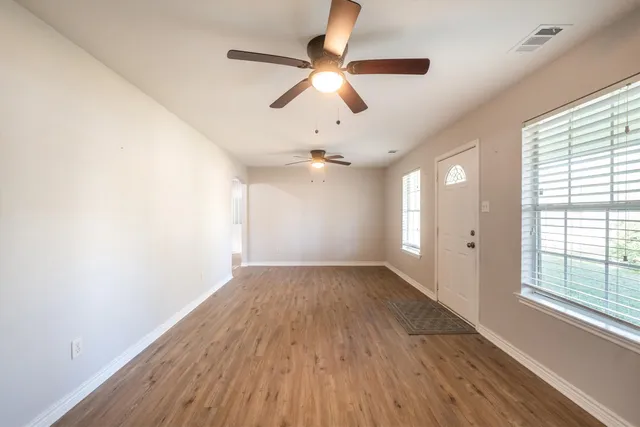 an empty room with wooden floor chandelier fan and windows