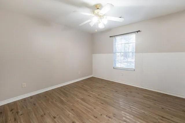 an empty room with wooden floor fan and windows