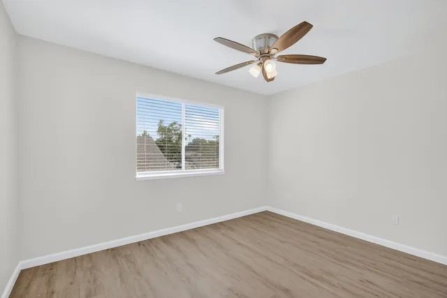 an empty room with wooden floor fan and windows