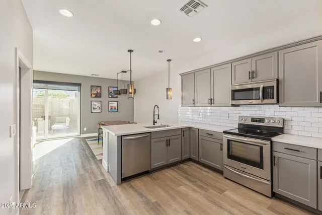 a kitchen with stainless steel appliances granite countertop a stove top oven a sink dishwasher a refrigerator and a microwave oven with wooden floor