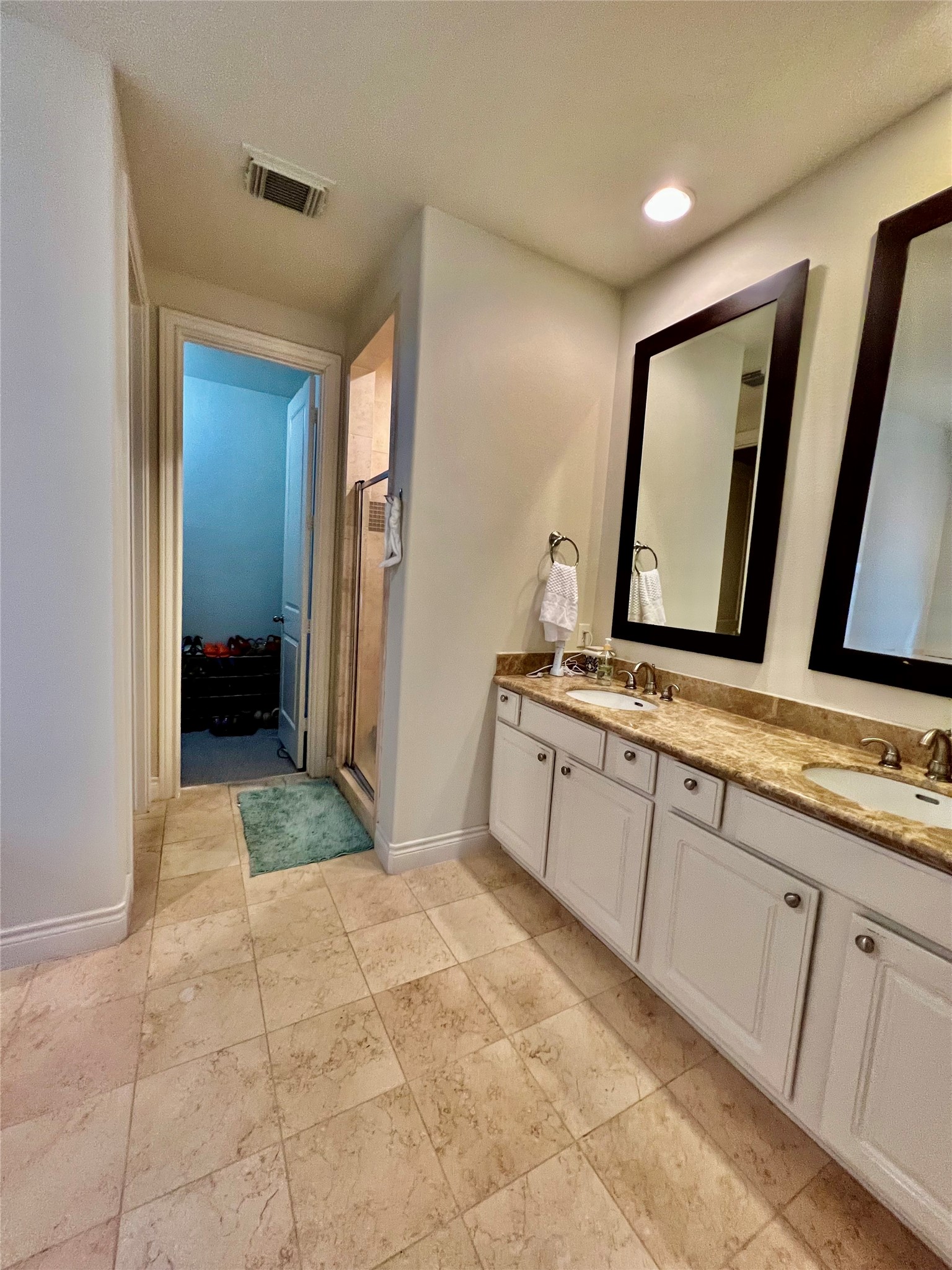 3255 Maxroy Street Houston, TX 77008 - Photo 22 of 26 This bathroom features a dual-sink vanity with granite countertops, large mirrors, and ample cabinetry. It has a walk-in shower and is connected to a closet area, with neutral tile flooring throughout.