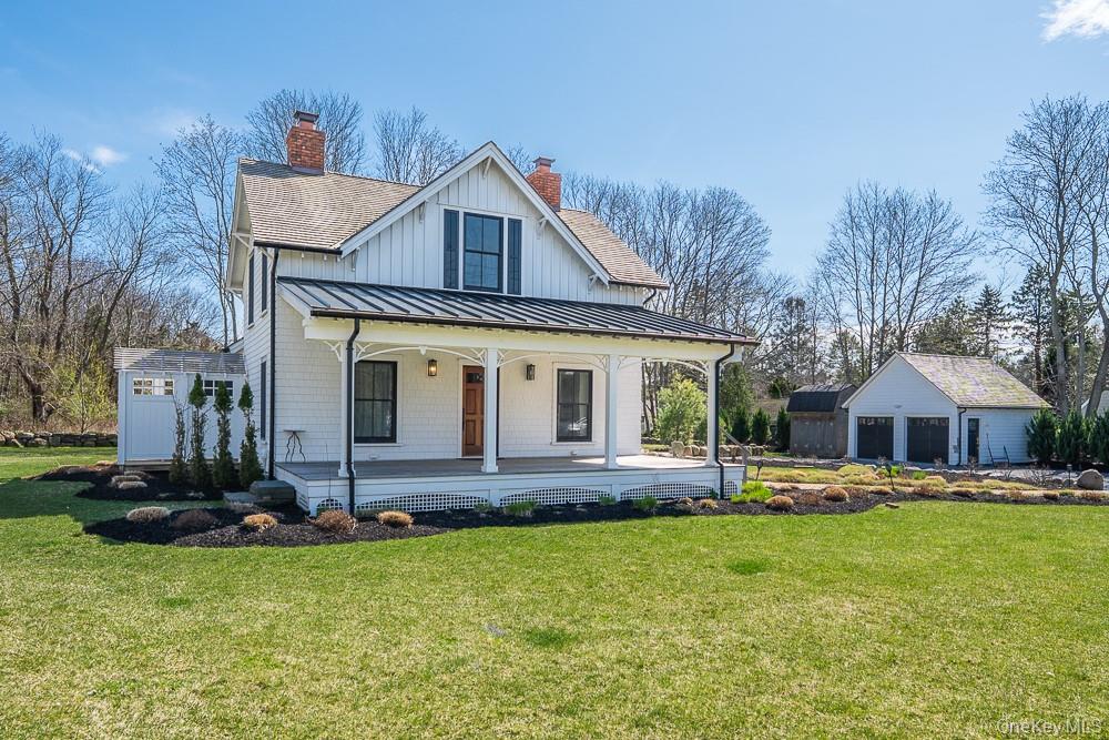 View of front facade with a standing seam roof, covered porch, a chimney, a front lawn, and roof with shingles