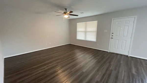 a view of an empty room with wooden floor and a window