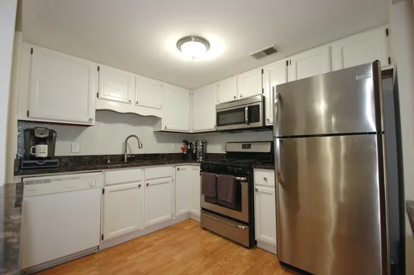a kitchen with stainless steel appliances granite countertop a refrigerator a stove a sink and white cabinets