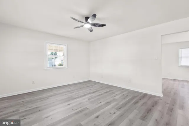 an empty room with wooden floor chandelier fan and windows