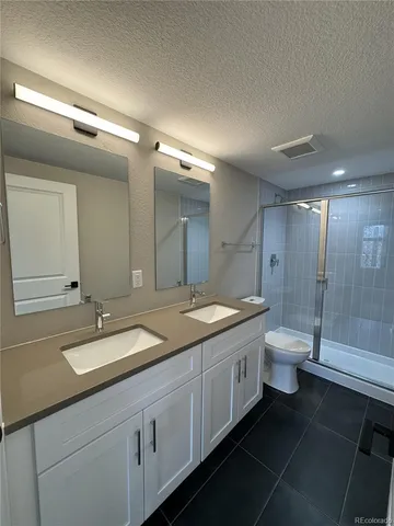 a bathroom with a granite countertop toilet a double vanity sink and a mirror