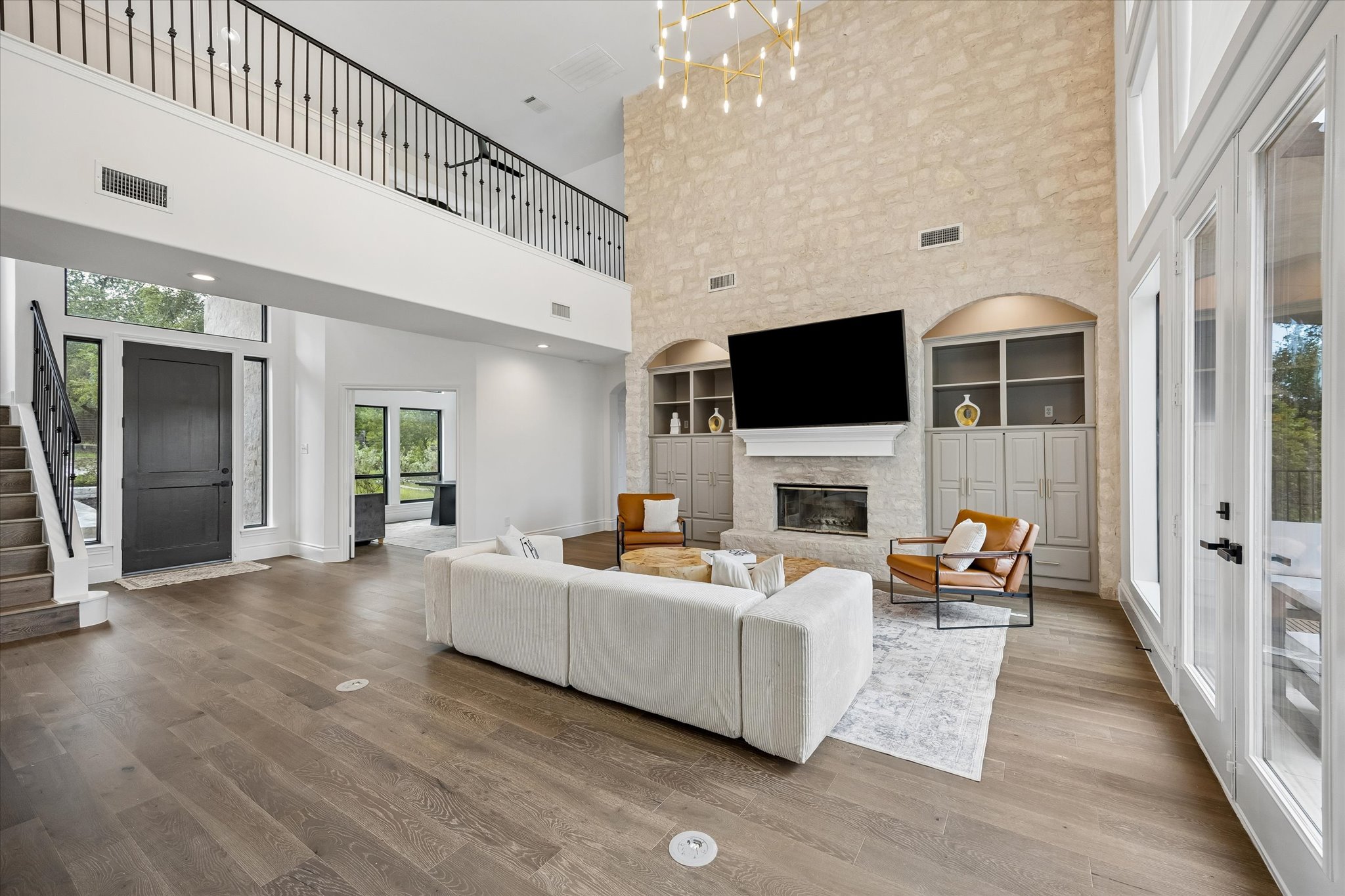 3719 Bee Creek Road Spicewood, TX 78669 - Photo 7 of 40 A grand, naturally illuminated living space features towering ceilings and hardwood floors, anchored by a prominent stone fireplace.