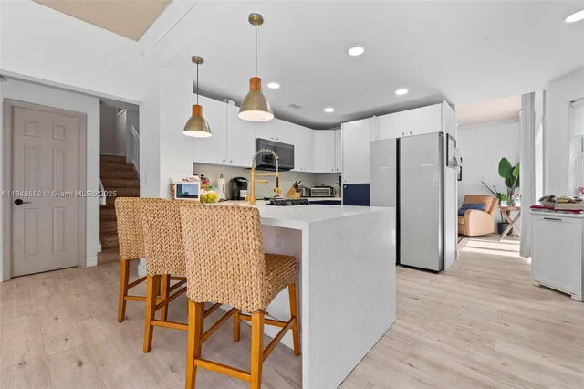 a kitchen with stainless steel appliances a refrigerator a stove a sink a dining table and chairs with wooden floor