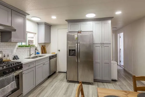 a kitchen with stainless steel appliances granite countertop a refrigerator a sink a stove and white cabinets with wooden floor
