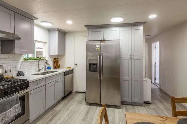 a kitchen with stainless steel appliances granite countertop a refrigerator a sink a stove and white cabinets with wooden floor