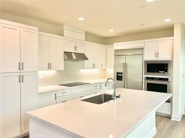 a kitchen with stainless steel appliances a sink a stove a refrigerator with white cabinets and wooden floor