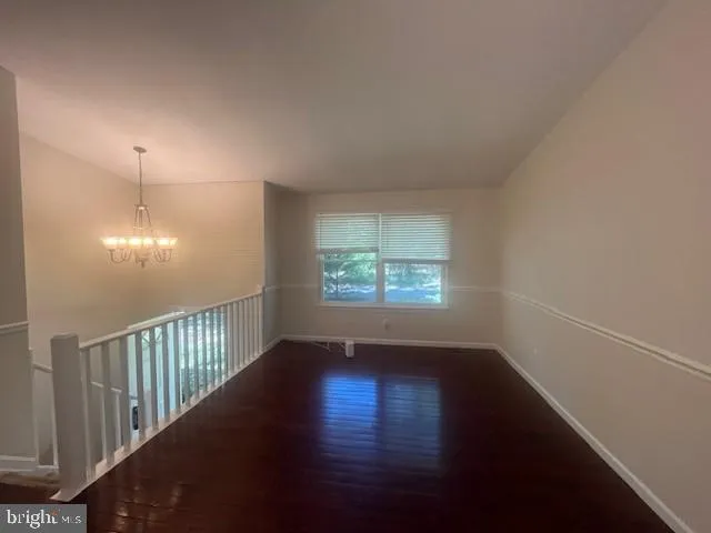 an empty room with wooden floor chandelier fan and windows