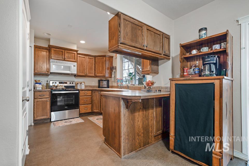 1230 East Main Street Weiser, ID 83672 - Photo 5 of 25 Kitchen featuring brown cabinets, stainless steel range with electric stovetop, white microwave, a kitchen bar, and a peninsula