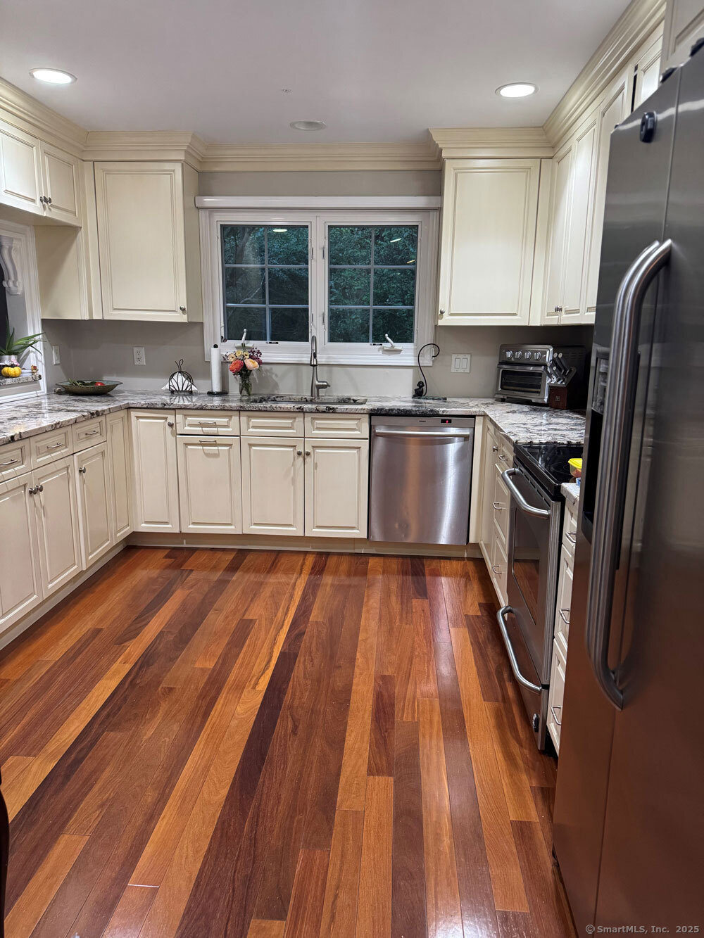 a kitchen with stainless steel appliances granite countertop a refrigerator a sink dishwasher a stove and white countertops with wooden floor