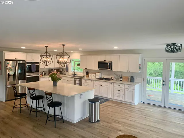 a kitchen with stainless steel appliances granite countertop a stove top oven a refrigerator a sink dishwasher a dining table and chairs with wooden floor