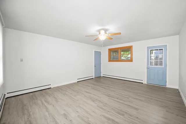 an empty room with wooden floor chandelier fan and windows