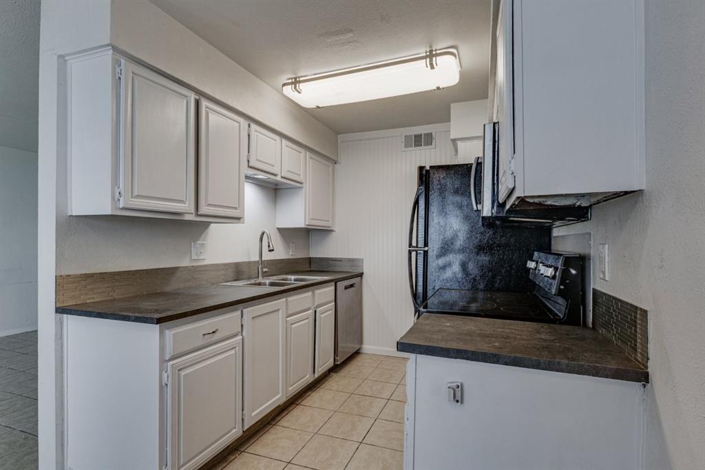 4606 Chaha Road, Unit 105 Garland, TX 75043 - Photo 11 of 26 Kitchen featuring dark countertops, appliances with stainless steel finishes, light tile patterned flooring, white cabinets, and a textured wall