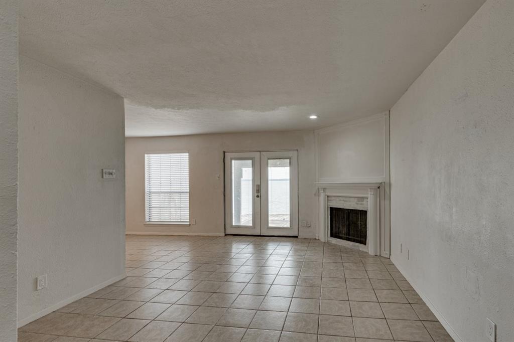 4606 Chaha Road, Unit 105 Garland, TX 75043 - Photo 5 of 26 Unfurnished living room with a textured wall, french doors, light tile patterned floors, a fireplace, and a textured ceiling