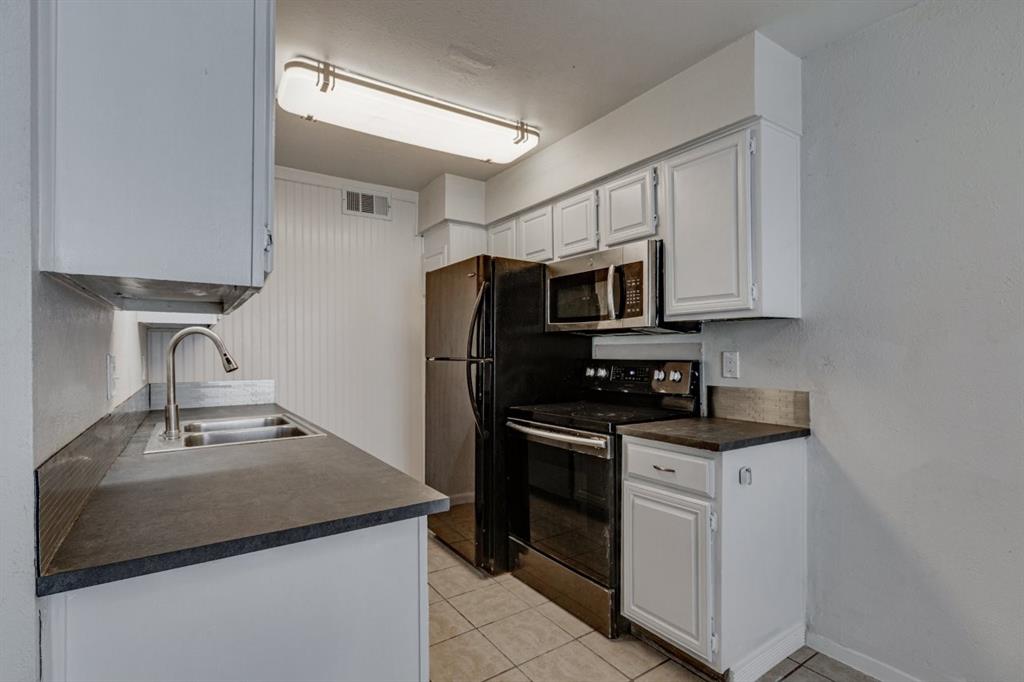 4606 Chaha Road, Unit 105 Garland, TX 75043 - Photo 10 of 26 Kitchen featuring dark countertops, black range with electric cooktop, light tile patterned floors, stainless steel microwave, and white cabinets