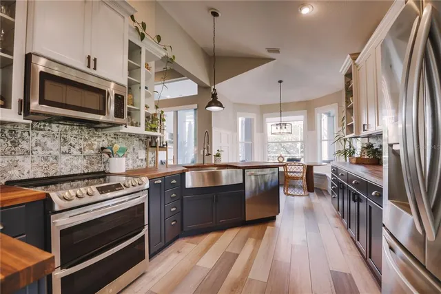 a kitchen with stainless steel appliances a stove a sink dishwasher a microwave oven and a dining table with wooden floor