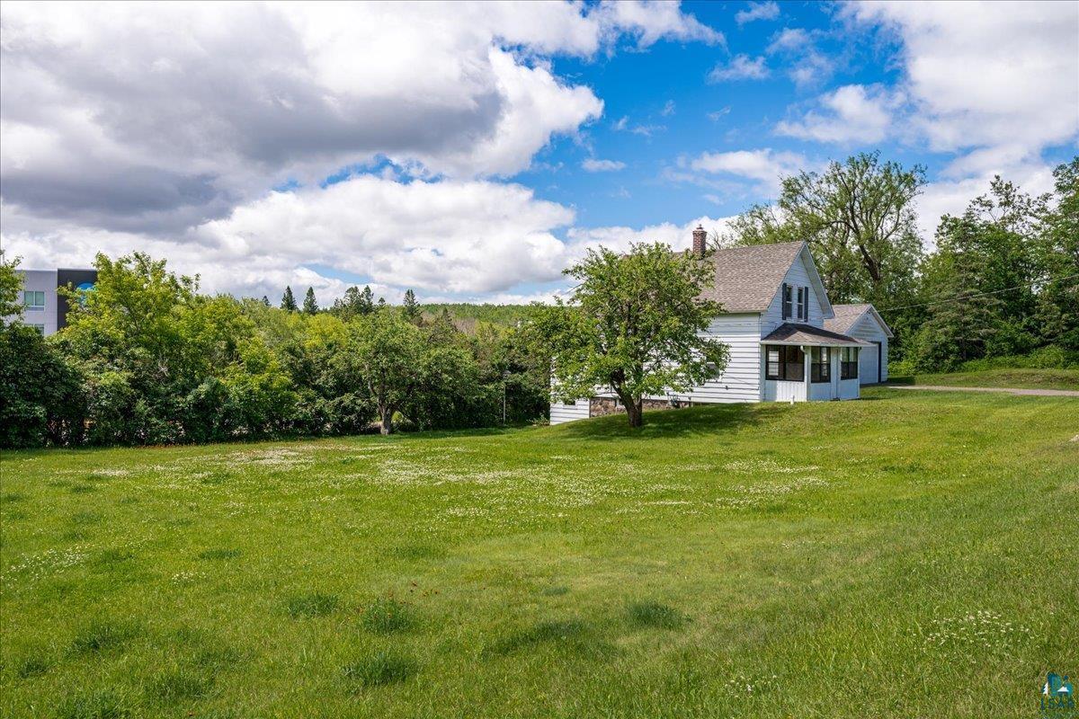 424 East Upham Road Duluth, MN 55811 - Photo 26 of 38 Expansive verdant lawn with a charming white clapboard residence featuring a gabled roof, a covered front porch, a prominent brick chimney, and dark window shutters
