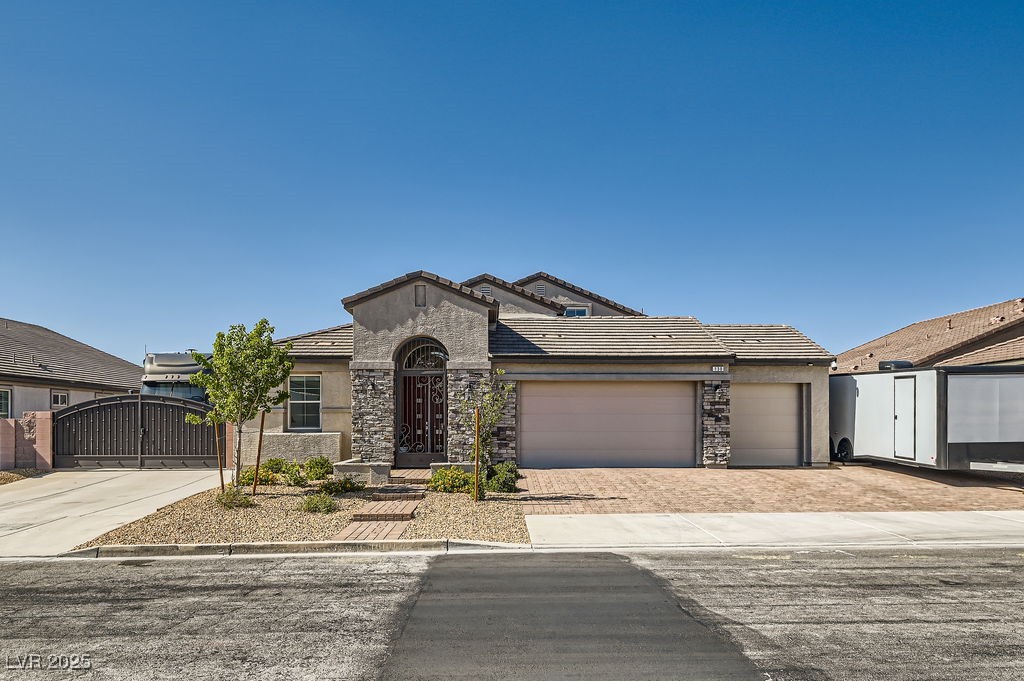 View of front facade featuring driveway, a tile roof, stone siding, and stucco siding