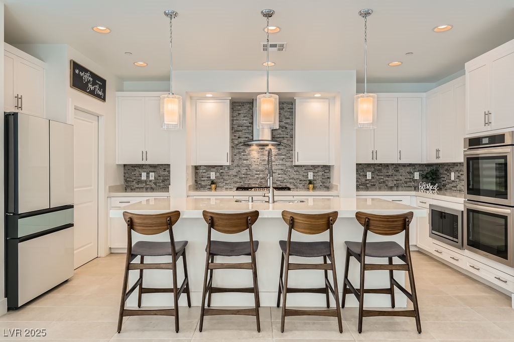 130 West Fairway Road Henderson, NV 89015 - Photo 13 of 40 Kitchen featuring stainless steel appliances, pendant lighting, white cabinetry, tasteful backsplash, and an island with sink
