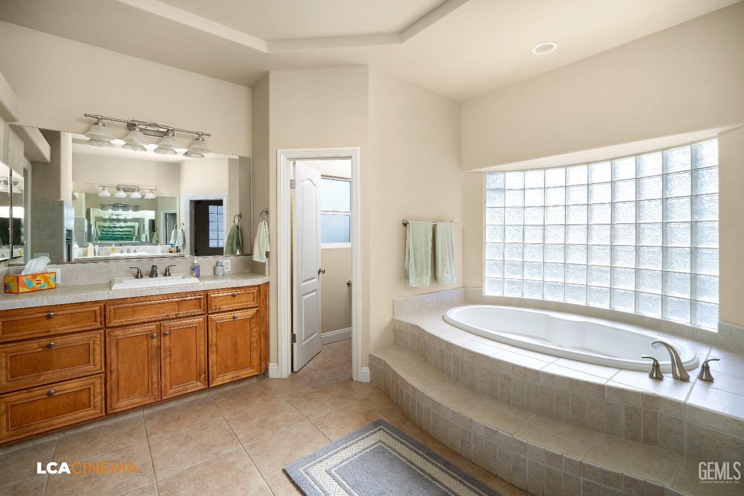 Undisclosed Address Bakersfield, CA 93314 - Photo 41 of 71 a spacious bathroom with double vanity a large mirror a bathtub and next to a window