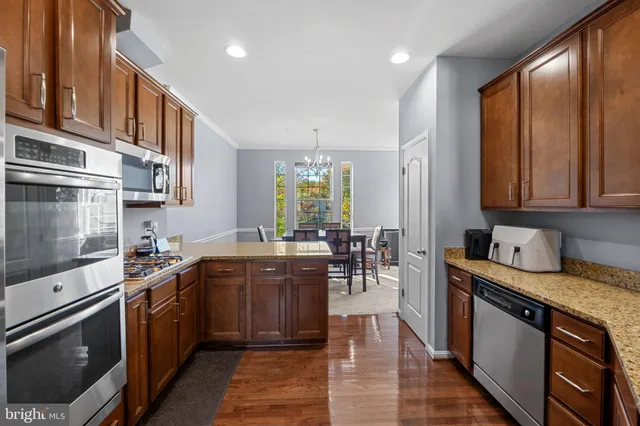 a kitchen with stainless steel appliances granite countertop wooden cabinets a sink a stove a dining table and chairs