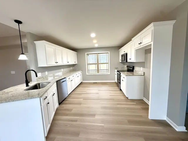 a large kitchen with stainless steel appliances granite countertop a stove a sink and white cabinets