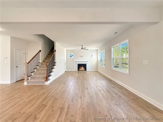 a view of an empty room with wooden floor fireplace and a window