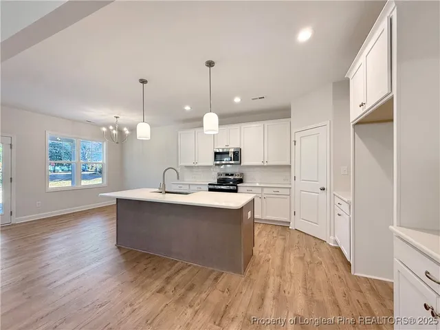 a large kitchen with white cabinets a sink dishwasher a dining table and chairs with wooden floor