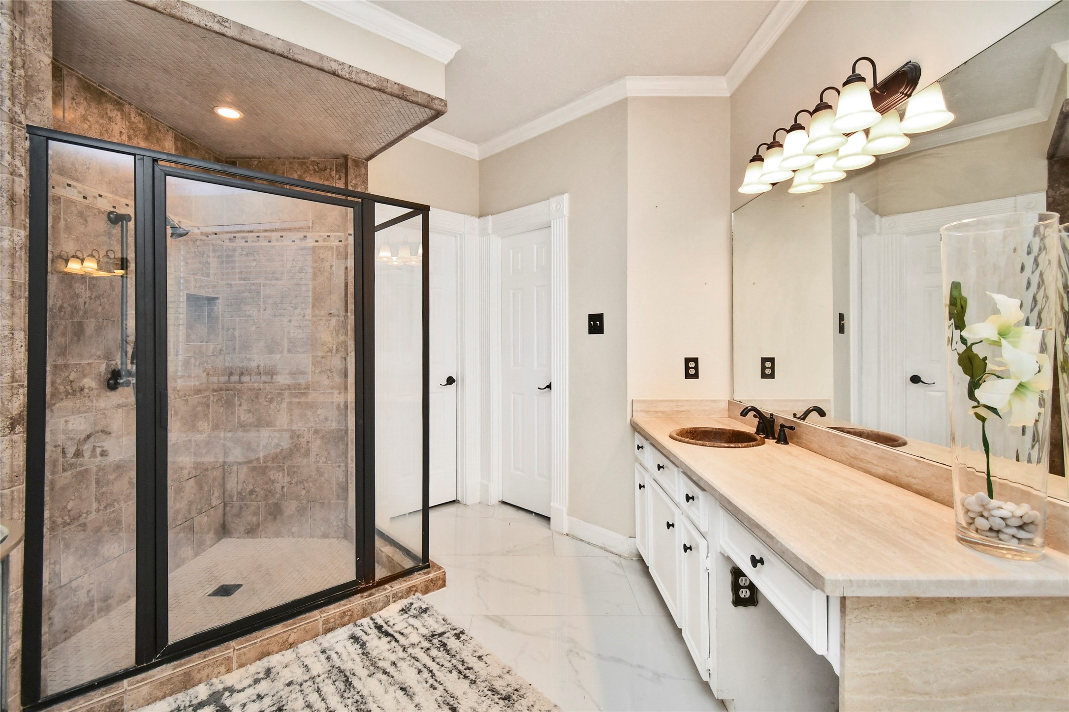 17311 Rothko Lane Spring, TX 77379 - Photo 23 of 37 Elegant bathroom featuring a spacious glass-enclosed shower with natural stone tiles, dual sinks with a sleek countertop, and stylish lighting fixtures.
