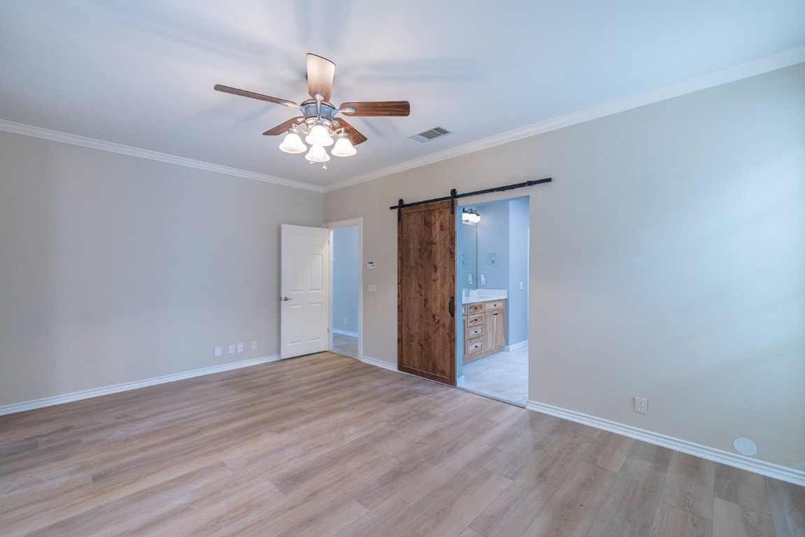8514 Racine Trail Austin, TX 78717 - Photo 23 of 33 Unfurnished bedroom featuring ornamental molding, a barn door, light wood-style floors, ceiling fan, and connected bathroom