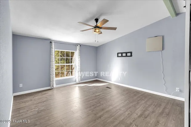 an empty room with wooden floor fan and windows