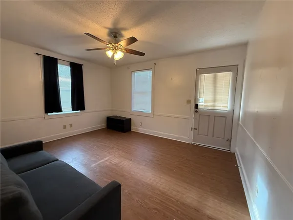 a view of an empty room with wooden floor and a ceiling fan