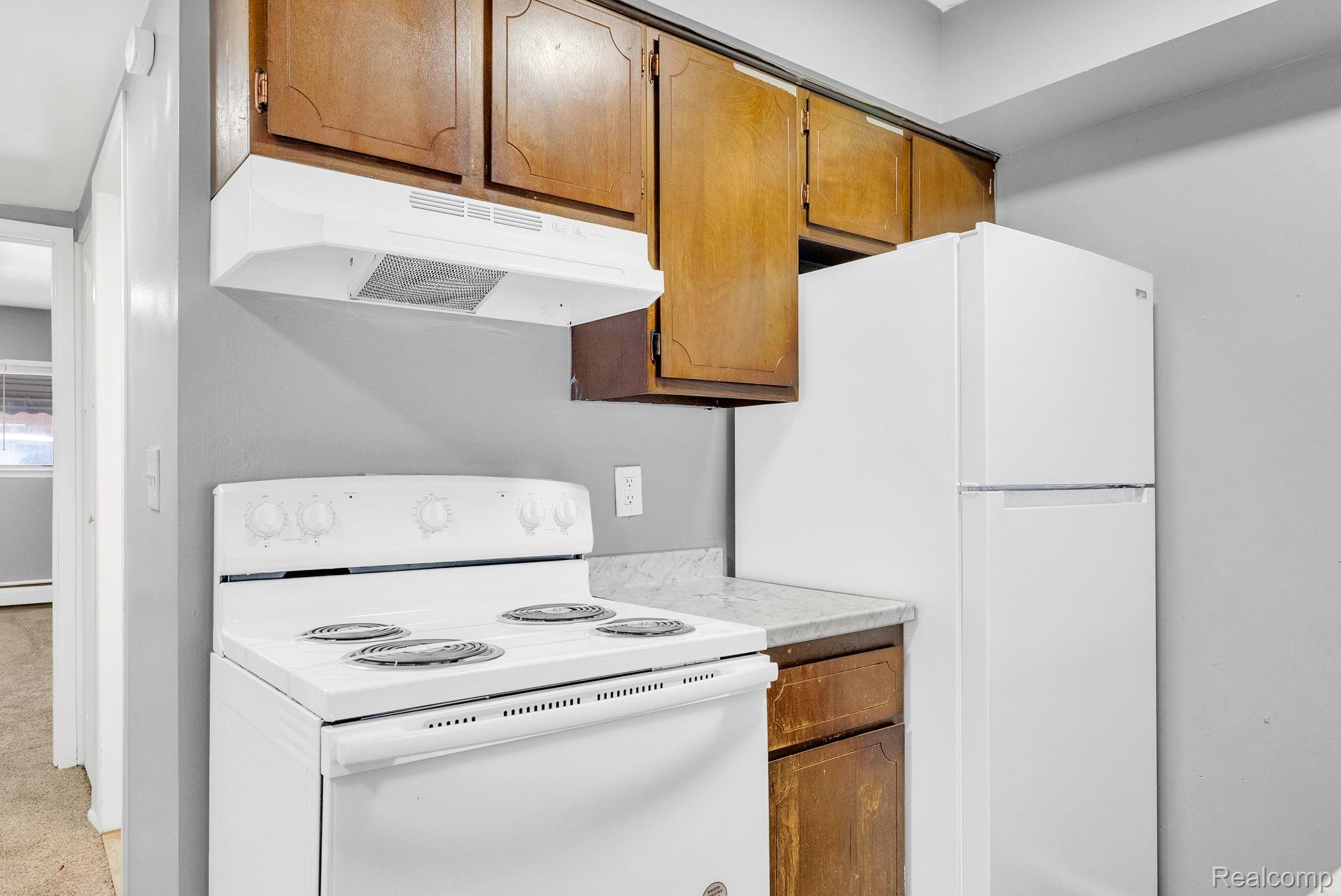 4535 Cadieux Road, Unit 42 / 210 Detroit, MI 48224 - Photo 11 of 16 Kitchen featuring white appliances, light countertops, brown cabinets, and under cabinet range hood
