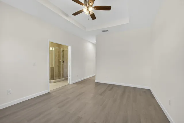 an empty room with wooden floor chandelier fan and windows