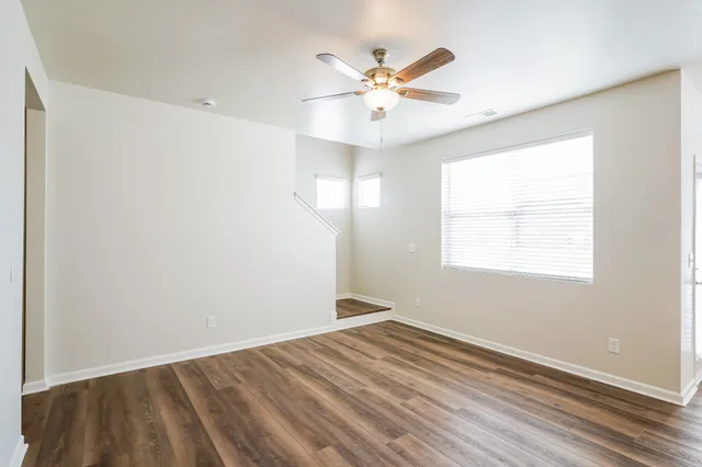 an empty room with wooden floor fan and windows