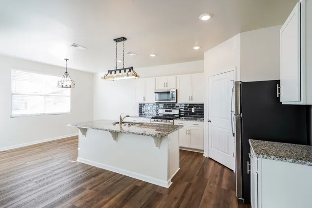 a kitchen with kitchen island white cabinets a refrigerator a stove a microwave and wooden floors