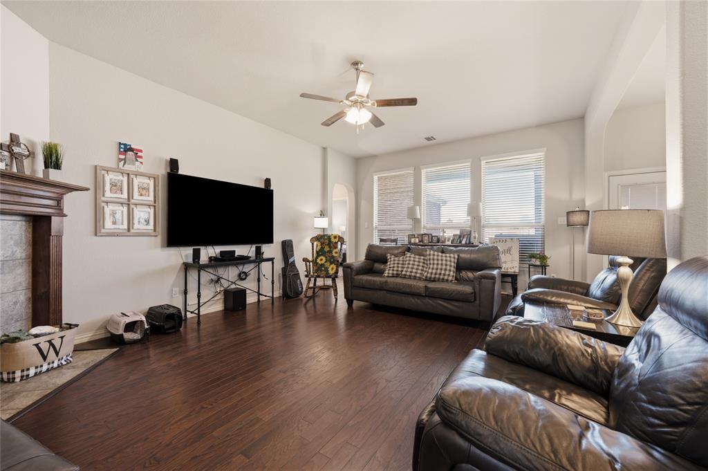 140 Chestnut Road Waxahachie, TX 75165 - Photo 7 of 26 Spacious living area featuring rich wood-finish flooring, a decorative fireplace with a substantial mantel, a ceiling fan with integrated lighting, and multiple large windows providing ample natural light