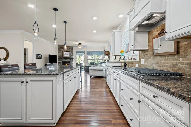a large kitchen with stainless steel appliances granite countertop a stove a sink dishwasher and white cabinets with wooden floor