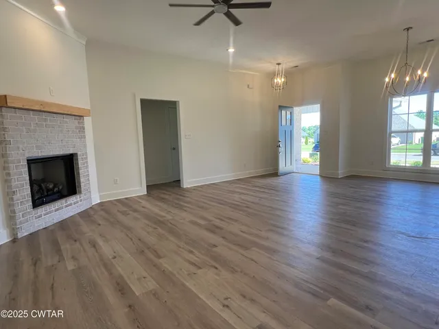 an empty room with wooden floor a fireplace a ceiling fan and windows