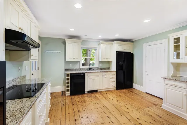 a kitchen with stainless steel appliances kitchen island granite countertop a refrigerator oven a sink dishwasher and white cabinets with wooden floor