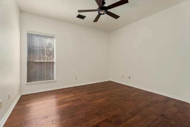 an empty room with wooden floor fan and windows