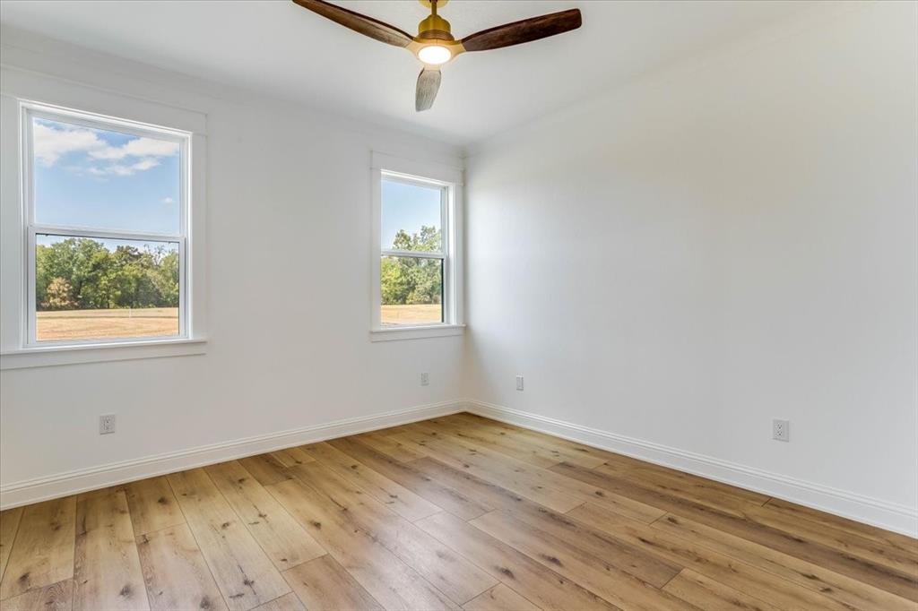 242 Private Road Mount Pleasant, TX 75455 - Photo 28 of 40 Two windows with white trim, wood-finish flooring, and a ceiling fan with wood blades