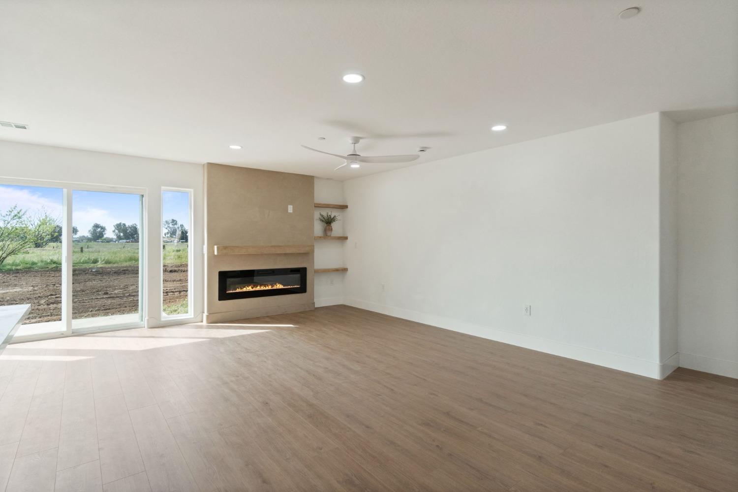 25918 Tanforan Drive Madera, CA 93638 - Photo 8 of 37 an empty room with wooden floor fireplace and windows